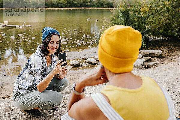 Lächelnde junge Frau  die Fotos einer Freundin vor dem See anklickt