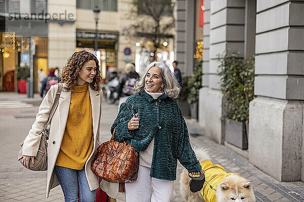 Lächelnde junge Frau geht mit Großmutter und Hund am Fußweg spazieren