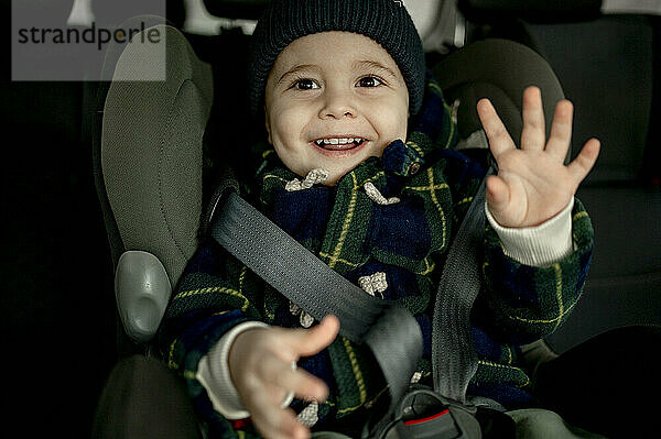 Smiling cute boy sitting in safety seat gesturing in car