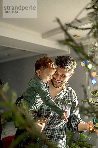 Lächelnder Sohn und Vater schmücken zu Hause den Weihnachtsbaum