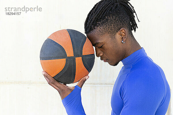 Young man holding basketball in front of wall