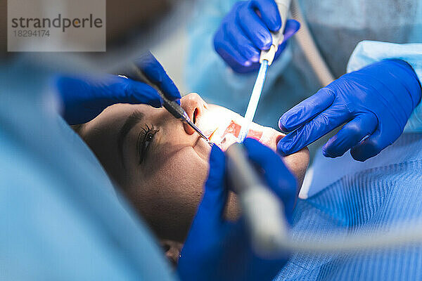 Junger Zahnarzt mit Assistent  der den Patienten in der Klinik untersucht