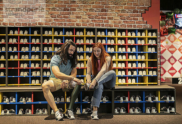 Mann hilft junger Frau beim Schuhebinden auf der Bowlingbahn