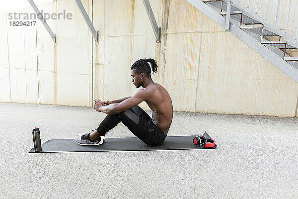 Shirtless man using smart phone on exercise mat