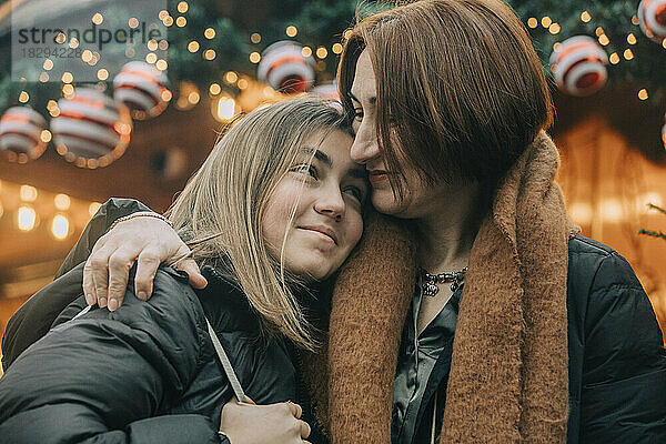 Glückliche Mutter mit Arm um Tochter auf dem Weihnachtsmarkt