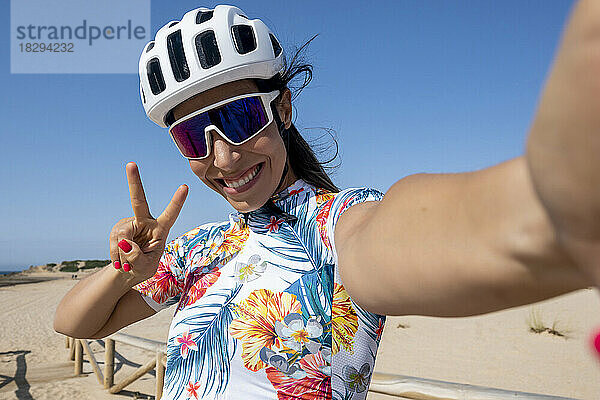 Glücklicher Radfahrer mit Helm  der eine Friedensgeste zeigt und ein Selfie macht