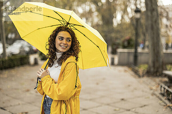Glückliche schöne Frau mit gelbem Regenschirm  die am Fußweg steht