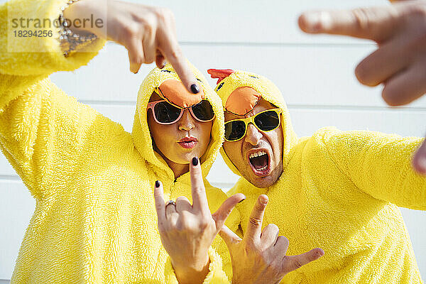 Freunde in gelben Hühnerkostümen gestikulieren im Freien