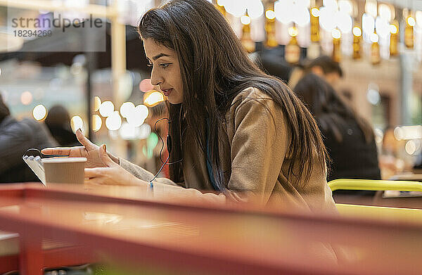 Frau mit In-Ear-Kopfhörern nutzt Tablet-PC im Café