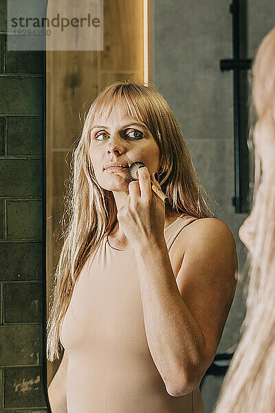 Frau trägt zu Hause im Badezimmer Make-up mit Pinsel auf