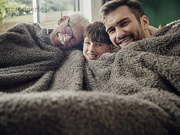 Glücklicher Großvater  Vater und Sohn kuscheln unter einer Decke auf der Couch im Wohnzimmer