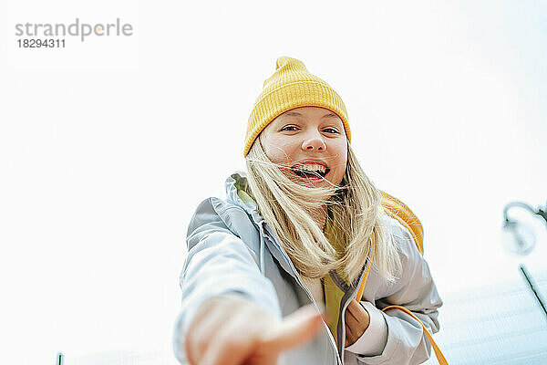 Cheerful blond girl gesturing under sky