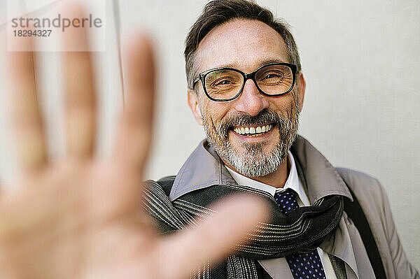 Happy mature businessman gesturing in front of wall