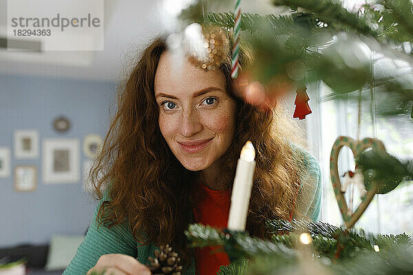 Lächelnde Frau schaut zu Hause durch den Weihnachtsbaum