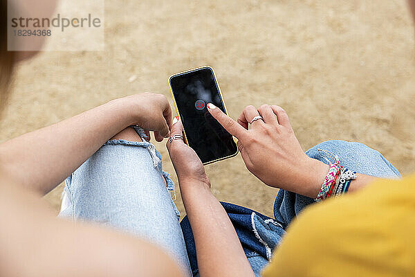 Hände einer Frau  die ihr Smartphone von einer Freundin im Park benutzt