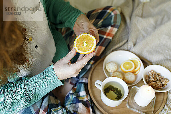 Frau hält eine Orangenscheibe in der Hand und sitzt zu Hause im Bett