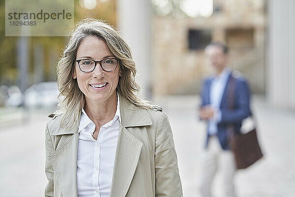 Lächelnde reife Geschäftsfrau mit Brille steht auf Fußweg