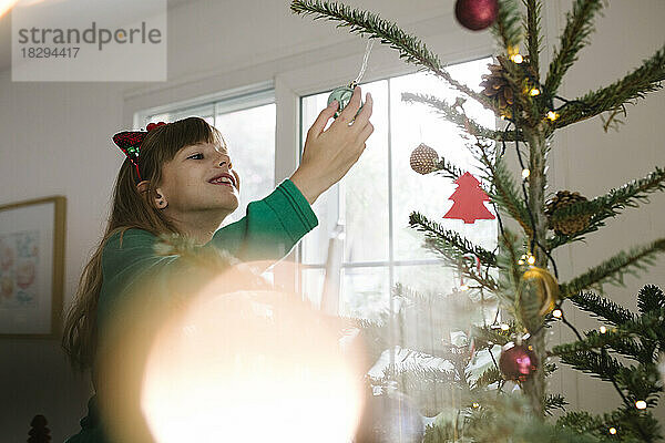 Lächelndes Mädchen mit einer Kugel  die zu Hause am Weihnachtsbaum hängt