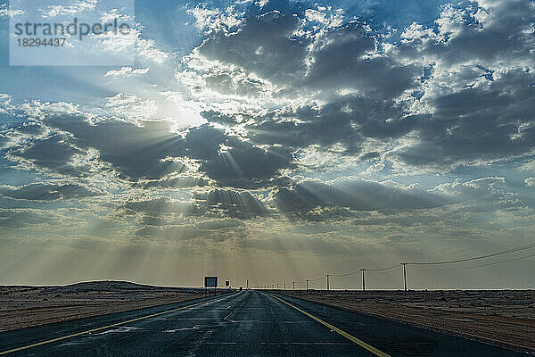 Saudi Arabia  Al-Ula  Setting sun piercing clouds over empty highway