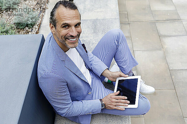 Glücklicher reifer Geschäftsmann mit Tablet-PC  der auf der Bank sitzt