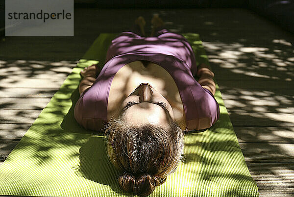 Junge Frau macht Yoga und liegt auf einer Trainingsmatte im Sonnenlicht