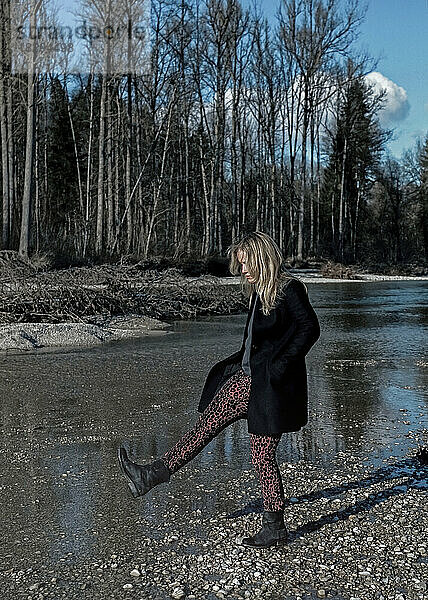 Frau spielt im Winter mit Steinen am Flussufer