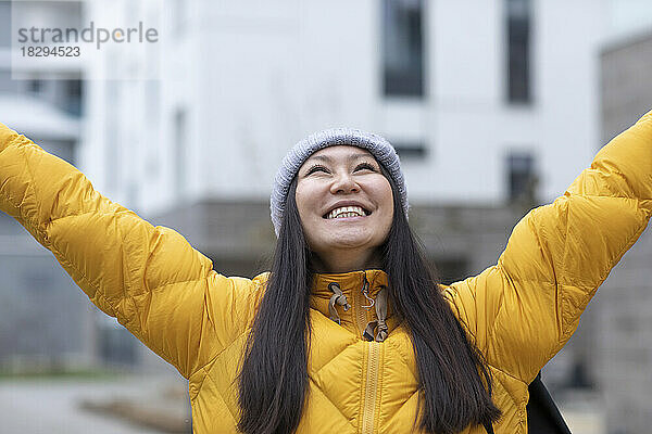 Happy woman wearing knit hat standing with arms raised