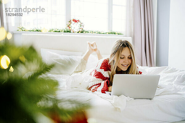 Glückliches Mädchen  das zu Hause mit Laptop im Bett liegt