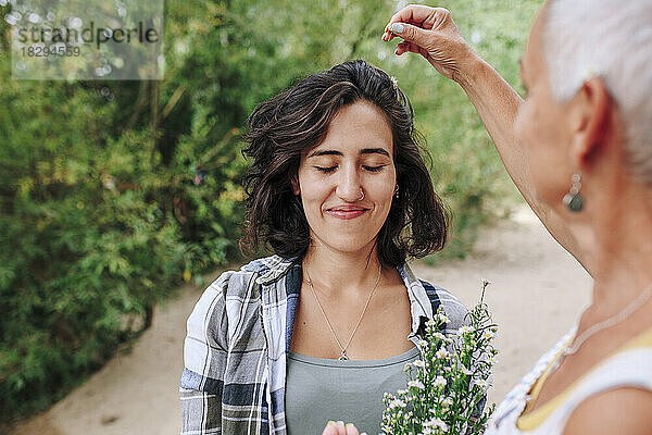 Ältere Frau legt Blumen auf die Haare einer Freundin im Park