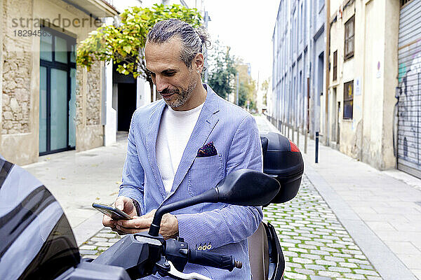 Reifer Geschäftsmann benutzt Mobiltelefon auf Motorrad sitzend