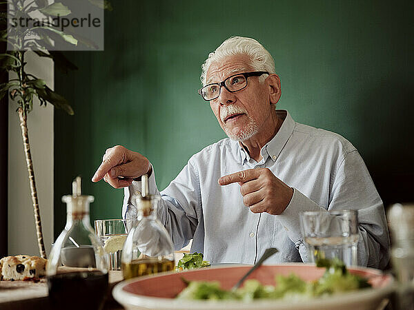 Weißhaariger Mann sitzt gestikulierend am Mittagstisch