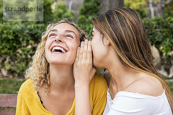 Woman whispering into friend's ear in park