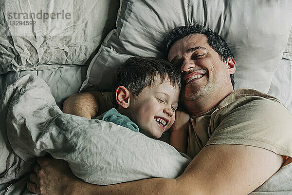Happy father and son lying on bed in bedroom