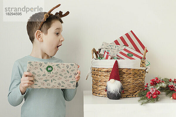 Netter Junge betrachtet Adventsgeschenke im Korb an der Wand