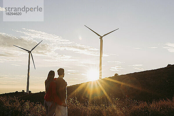 Händchen haltendes Paar blickt bei Sonnenuntergang auf den Windpark
