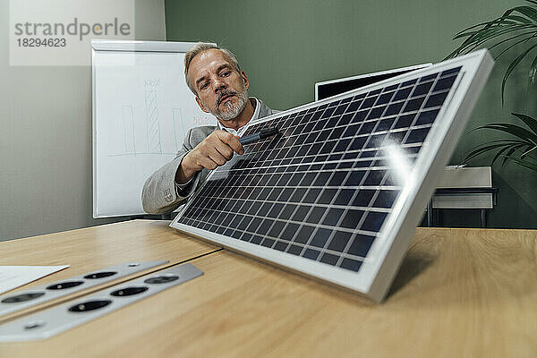 Reifer Geschäftsmann mit Solarpanel sitzt am Konferenztisch