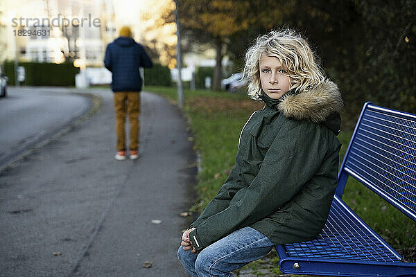 Blond boy sitting on bench at footpath