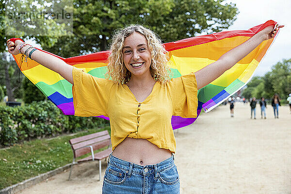 Glückliche lesbische junge Frau hält Regenbogenfahne im Park
