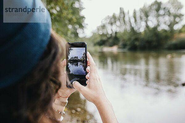 Frau klickt mit Smartphone am See im Park auf Fotos