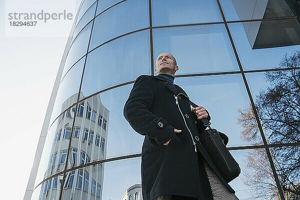 Reifer Geschäftsmann mit den Händen in den Taschen  der in der Nähe eines Glasgebäudes steht