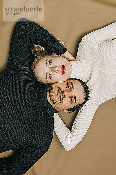 Couple lying down on brown backdrop