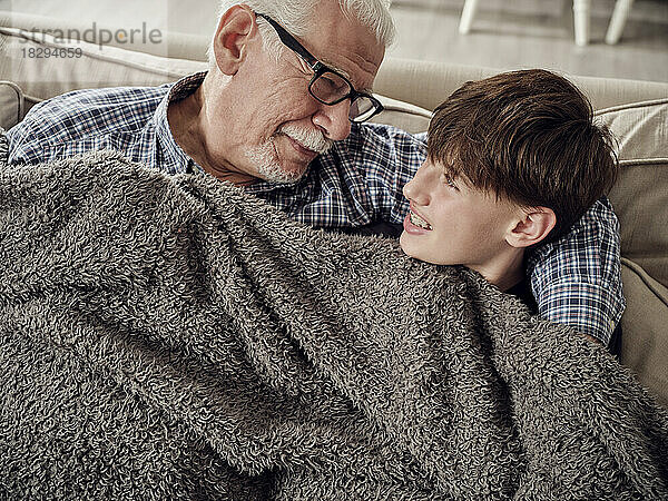 Großvater und Sohn kuscheln unter einer Decke auf der Couch im Wohnzimmer