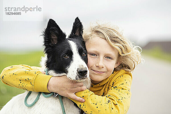 Lächelnder blonder Junge umarmt Border-Collie-Hund