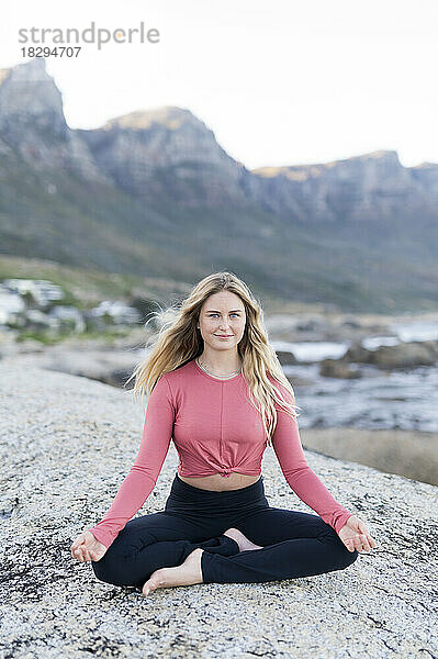 Lächelnde junge Frau meditiert auf einem Felsen