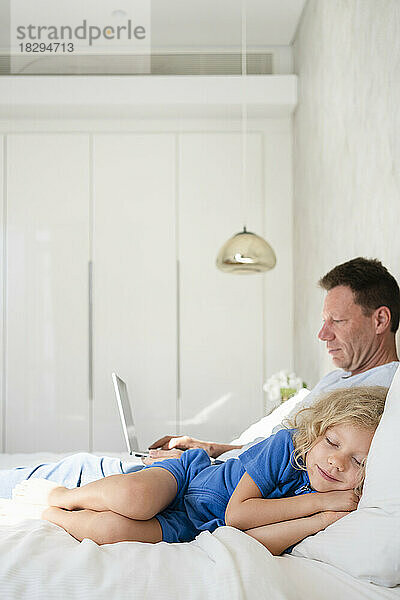 Mädchen schläft beim Vater mit Laptop im heimischen Bett