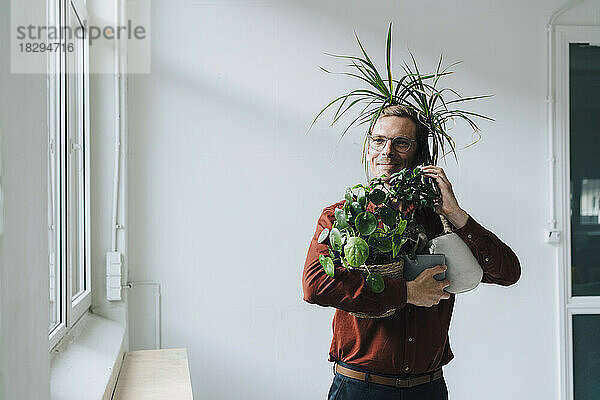 Geschäftsmann spricht mit Smartphone und steht mit Pflanzen vor der Wand