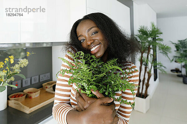Glückliche Frau umarmt Topfpflanze in der Küche