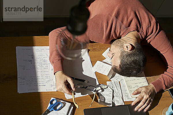 Müder Mann schläft auf Dokumenten am Schreibtisch