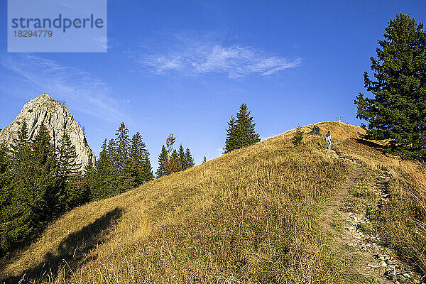 Mann wandert auf einem Berg über einen schmalen Fußweg unter blauem Himmel