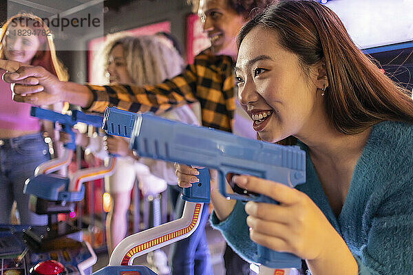 Happy young woman enjoying shooting game with friends at arcade